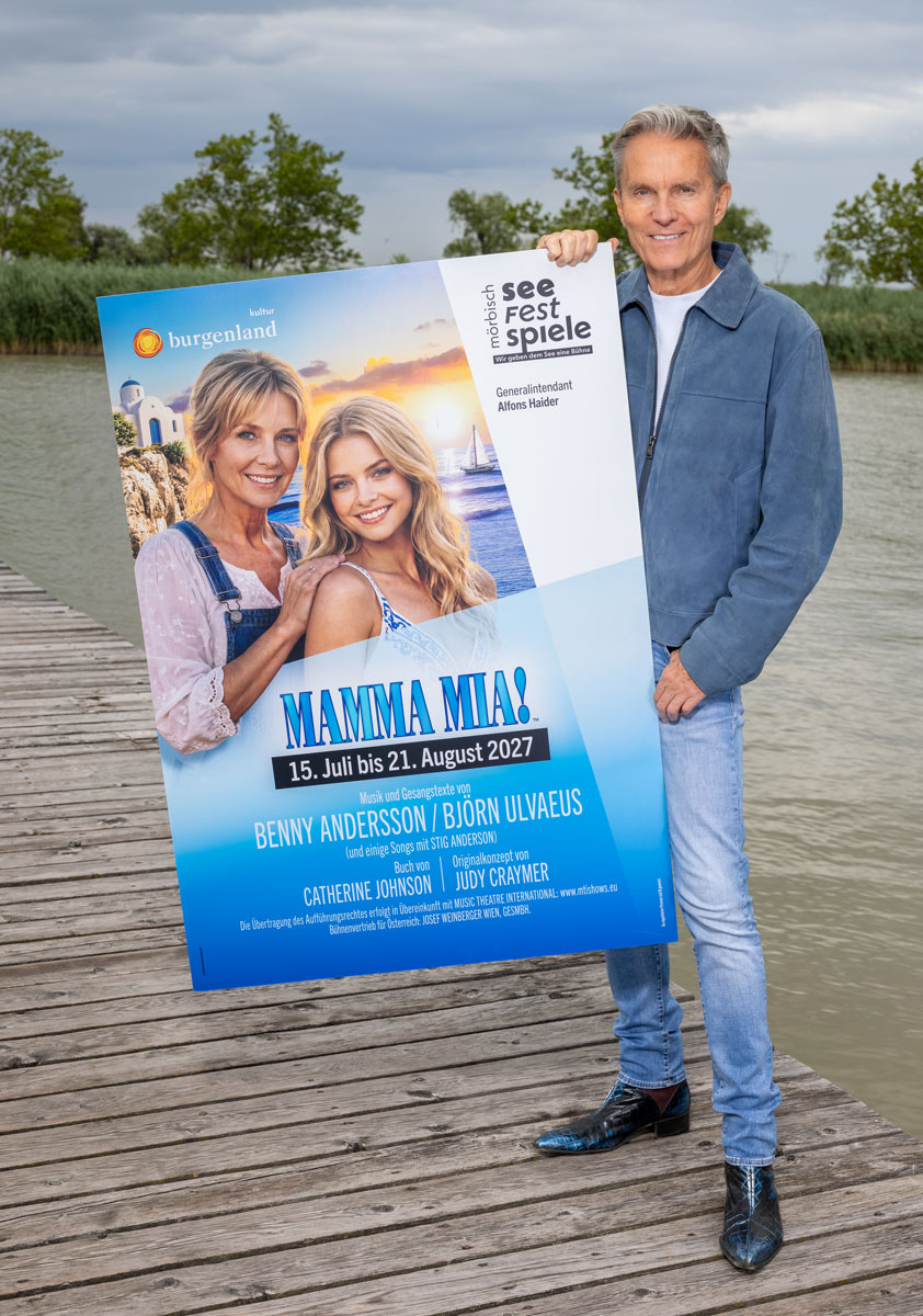 Alfons Haider auf einem Steg über dem Neusiedler See mit einem Plakat von MAMMA MIA.