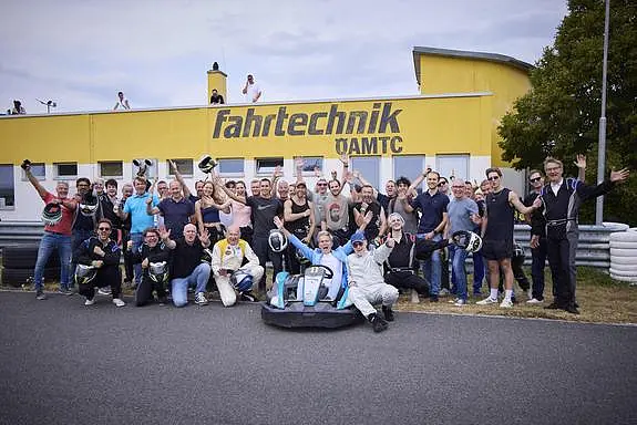 Gruppe von Menschen in Rennbekleidung und Zivil vor dem Fahrtechnikzentrum ÖAMTC in Greinbach.