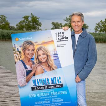 Alfons Haider auf einem Steg über dem Neusiedler See mit einem Plakat von MAMMA MIA.